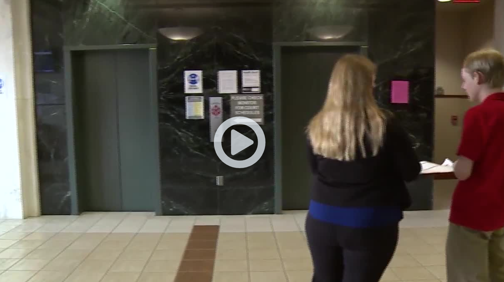 Screenshot of news story shows two volunteers standing outside an elevator