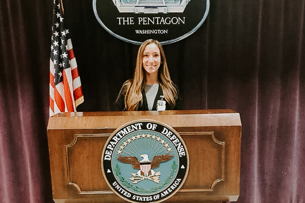 Student standing at a podium with the Department of Defense seat at the Pentagon.