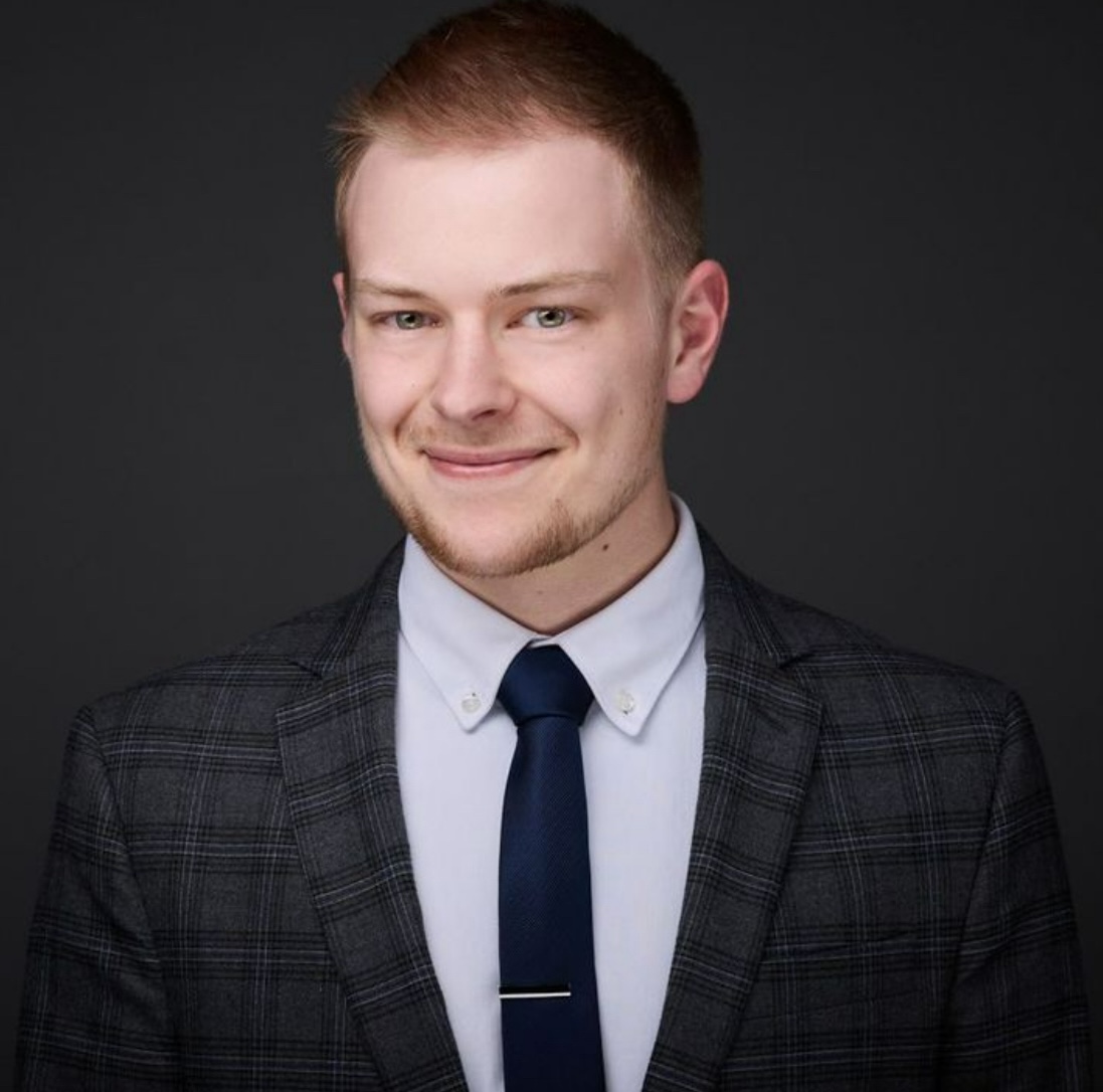 Headshot of Elliott, who is wearing a dark suit and tie and light colored shirt