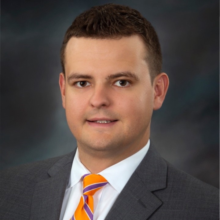 Headshot of John, who is wearing a dark suit jacket and orange tie