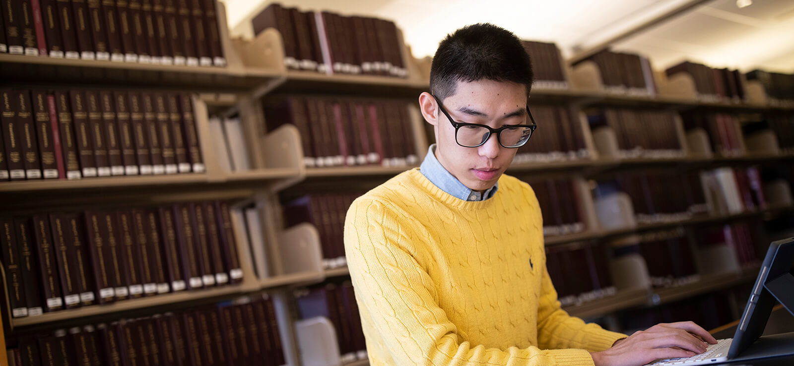 Student working on laptop in front of library bookshelves