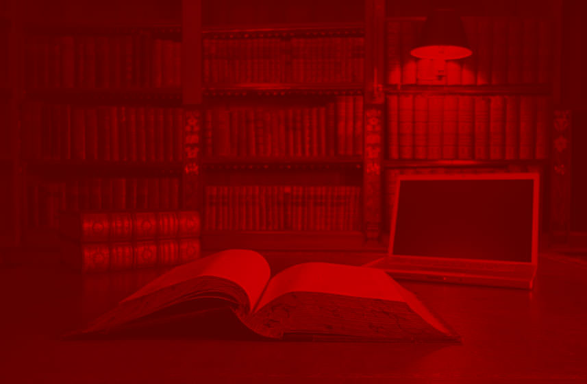 Open book and laptop on a desk in front of a bookshelf