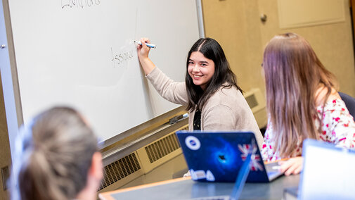 Student writing on whiteboard while looking at her peers