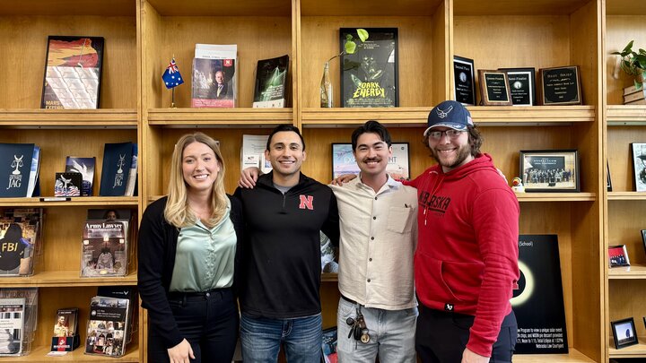 4 nebraska law students in front of some shelves in the law building
