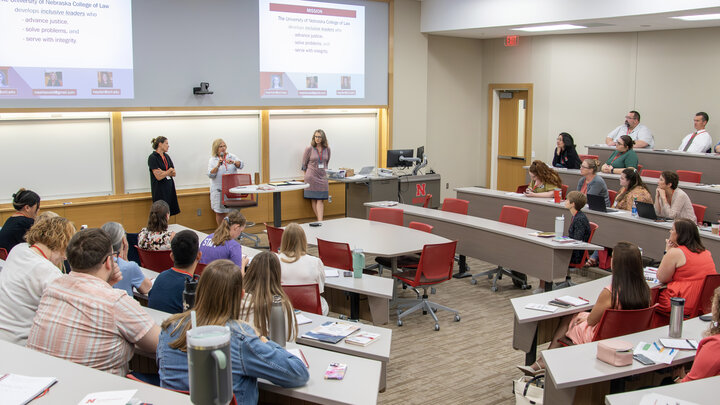 three women from the College of Law present to a full lecture room 