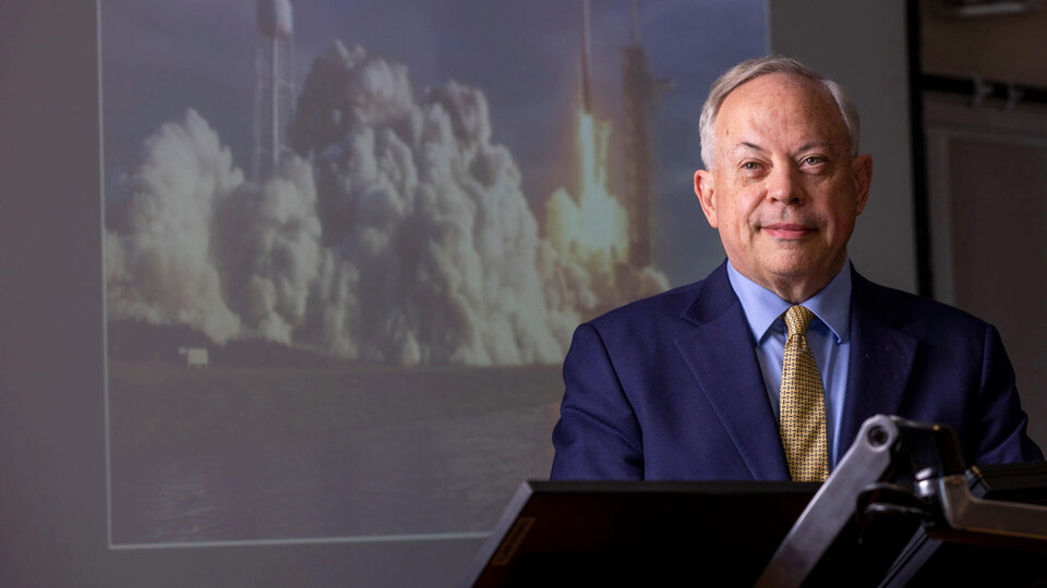 Professor Jack Beard smiling in front of projected rocket launch background