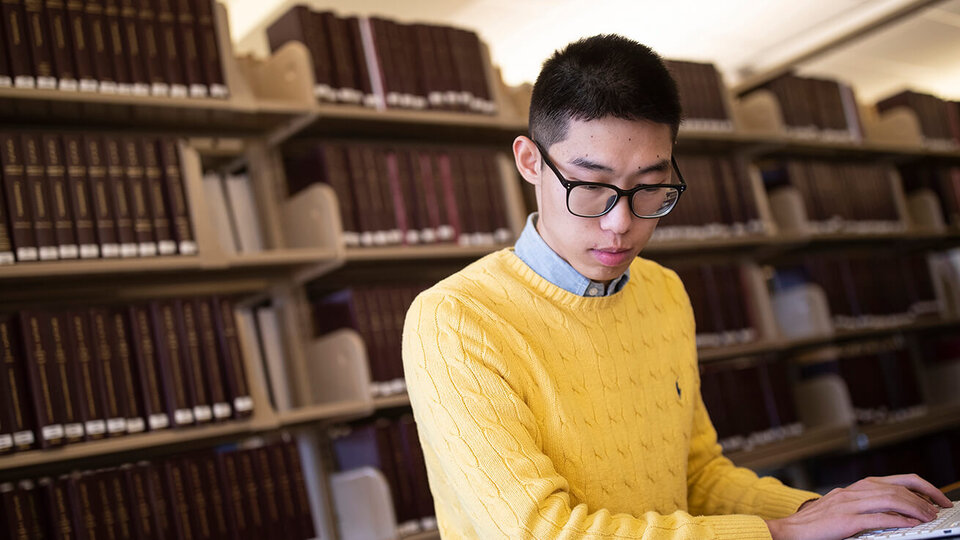 Student working on laptop in front of library bookshelves