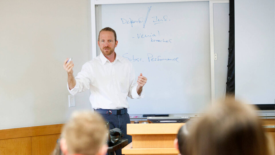 Professor Anthony Schutz holding a marker in his hand in front of a whiteboard and lecturing