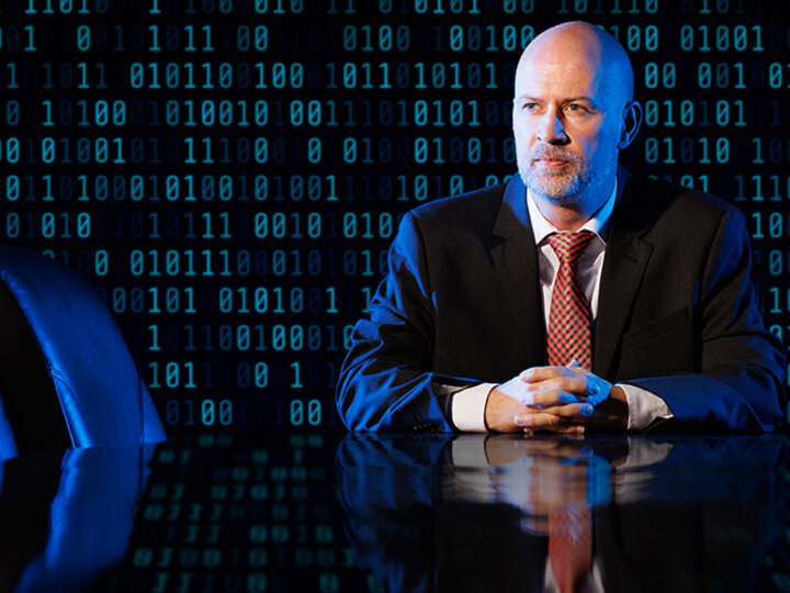 Paul Weitzel sitting at a conference table with binary code superimposed behind and around him