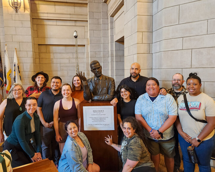 A number of Nebraska Appleseed staff, including Alison, are posing for a picture in the state capitol building with the bust of Malcolm X during his Nebraska Hall of Fame induction ceremony at the 