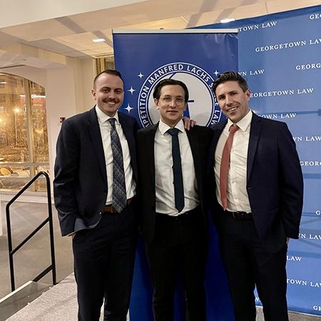 Student Grant Jones, Matias Cava, and Jon Natvig stand in front of Manfred Lachs Space Law Moot Court banner